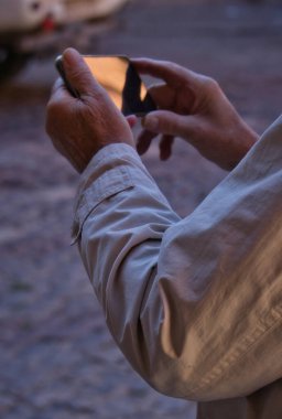 Sokakta cep telefonunu kullanan yaşlı bir adamın elinin yakın plan görüntüsü. Yaşlılar tarafından teknoloji kullanımı kavramı. Yaşlı adam teknolojiyi kullanıyor..