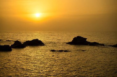 Kayalar sarı bir arka plana karşı. Denizde sıcak ve görkemli bir gün doğumu. Sakin, meditasyon, seyahat, yeni yıl, yeni hedefler, uyanma, mutluluk, yeni gün için teşekkürler.