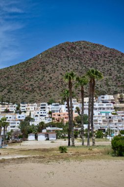 SAN JOSE, ALMERIA, İSPA: 25 Mayıs 2021: Güneşli bir günde, İspanya 'nın Almerya kentindeki Cabo de Gata' da çok ünlü bir turizm merkezi olan San Jose şehrinin panoramik manzarası. Dağ ve beyaz evler
