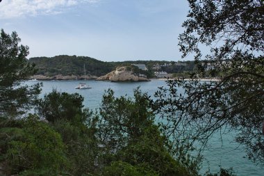 CALA GALDANA, Balearik Adaları, İspanya. 14 Nisan 2022: Güneşli bir öğleden sonra Cala Galdana 'nın kayalıklarının ve bazı yatların panoramik manzarası.