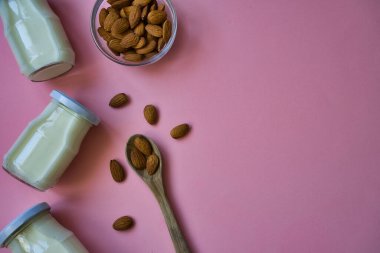 Pastel pembe arka planda cam kavanozlarda yulaf gevreği ve badem içeceği. Sağlıklı yaşam tarzı ve diyet konsepti. Üst Manzara. Metin için boşluk.