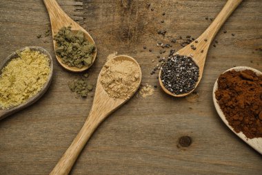 Tahta kaşıklar üzerinde süper yiyeceklerin kırsal bileşimi. Maca, Chia, Hemp Protein, saf kakao ve besin maya, hepsi vitamin ve omega-3 kaynağı. Sağlıklı yaşam tarzı ve diyet konsepti. Üst görünüm