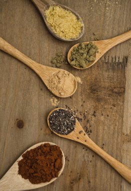 Tahta kaşıklar üzerinde süper yiyeceklerin kırsal bileşimi. Maca, Chia, Hemp Protein, saf kakao ve besin maya, hepsi vitamin ve omega-3 kaynağı. Sağlıklı yaşam tarzı ve diyet konsepti. Üst görünüm