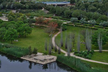 Bulutlu bir yaz gününde, büyük şehrin merkezindeki parkın panoramik manzarası. Ortasında bir göl ve yeşil ağaçlar var. Yağmurun nemli atmosferinde. Açık hava spor alanı