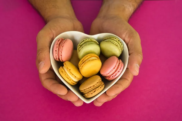Thank you gift with colorful macaroons inside a heart shaped box on hot pink background. Food concept