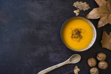 Kurumuş yapraklı güz kompozisyonu ve koyu arkaplanda ev yapımı lezzetli balkabağı çorbası. Boşluğu kopyala