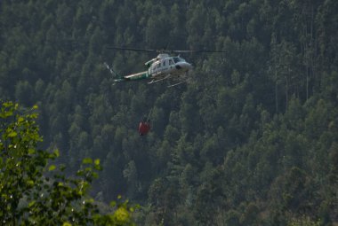 BUELLES, CANTABRIA, ESPanyA, JULIO 13, 2022: Su taşıyan bir kova Bambi ile itfaiye ve kurtarma helikopteri