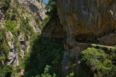 Route Cares (Cain-Poncebos), CANTABRIA, SPAIN, JULY, 12, 2022: Güneşli bir yaz gününde Cares yolunda doğal bir kaya kemerini geçen birkaç yürüyüşçü.