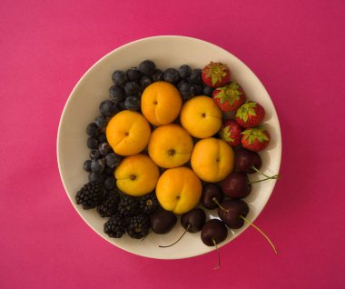 Taze böğürtlen çeşitliliği ve pembe arka planda organik yaz meyvesi. Sağlıklı yiyecekler. Kayısı, yabanmersini, yabanmersini ve kiraz. Lezzetli, tatlı, sulu ve fotokopi alanı olan olgun meyveler..