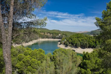Spectacular panoramic views of the Guadalhorce reservoir, next to the Caminito del Rey in Malaga, Andalusia, Spain. Turquoise blue water and forest with blue sky on a sunny day.