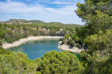 Spectacular panoramic views of the Guadalhorce reservoir, next to the Caminito del Rey in Malaga, Andalusia, Spain. Turquoise blue water and forest with blue sky on a sunny day.
