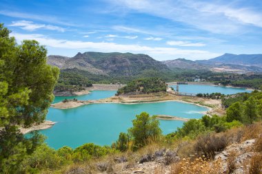 Spectacular panoramic views of the Guadalhorce reservoir, next to the Caminito del Rey in Malaga, Andalusia, Spain. Turquoise blue water and forest with blue sky on a sunny day.