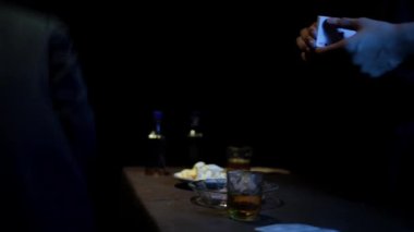 footage of man sitting at table with drinks and other man shuffling cards in cinematic light