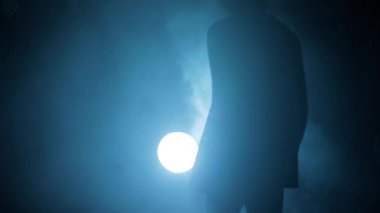 Elinde silahla dolaşan takım elbiseli bir gangsterin dramatik sinematik çekimi. Dramatik ışıkta yürüyen bir gangsterin siluetleri, duman bulutları. Yüksek çözünürlüklü görüntü. Yavaş Hareket.