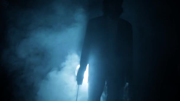 劇的な照明を過ぎて歩く彼の手とロープの斧で青いスーツの男のショット — ストック動画