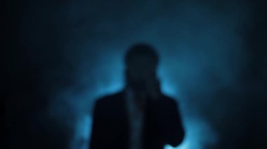 Defocused shot of a man (killer) in the suit with blood on his shirt, smoke, and dramatic light.