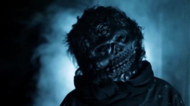 Cinematic shot of a man wearing a scary mask in dramatic light, with some fog.