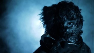 Cinematic shot of a man wearing a scary mask in dramatic light, with some fog.