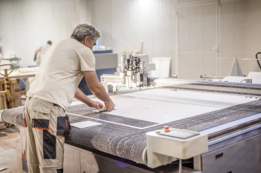 Fabrika işçi teknisyeni, kumaş tekstil malzemelerini kesmek için CNC dijital kesici makinesinde çalışıyor.