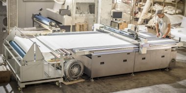 Fabrika işçi teknisyeni, kumaş tekstil malzemelerini kesmek için CNC dijital kesici makinesinde çalışıyor.