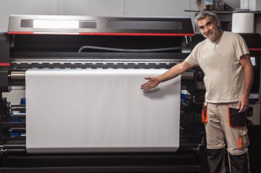 Teknisyen, dijital yazıcı ofisindeki büyük endüstriyel yazıcı ve çizer makinesinde beyaz kağıdın boş alanını gösteriyor ve gösteriyor.