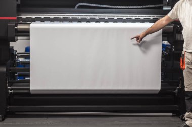 Teknisyen, dijital yazıcı ofisindeki büyük endüstriyel yazıcı ve çizer makinesinde beyaz kağıdın boş alanını gösteriyor ve gösteriyor.