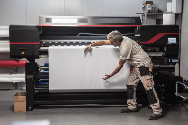 数字印刷车间大型工业打印机和绘图机上的技术人员操作员展示并指向空白空白空白白纸 — 图库照片