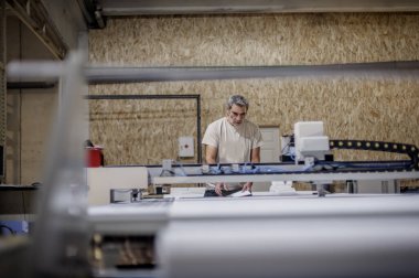 Fabrika işçi teknisyeni, kumaş tekstil malzemelerini kesmek için CNC dijital kesici makinesinde çalışıyor.
