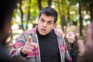 Kavga eden iki agresif, sinirli ve sinirli adam ve çatışmayı önlemeye çalışan bir kadın. Parmakla göstererek. Grup kavgası kavramı
