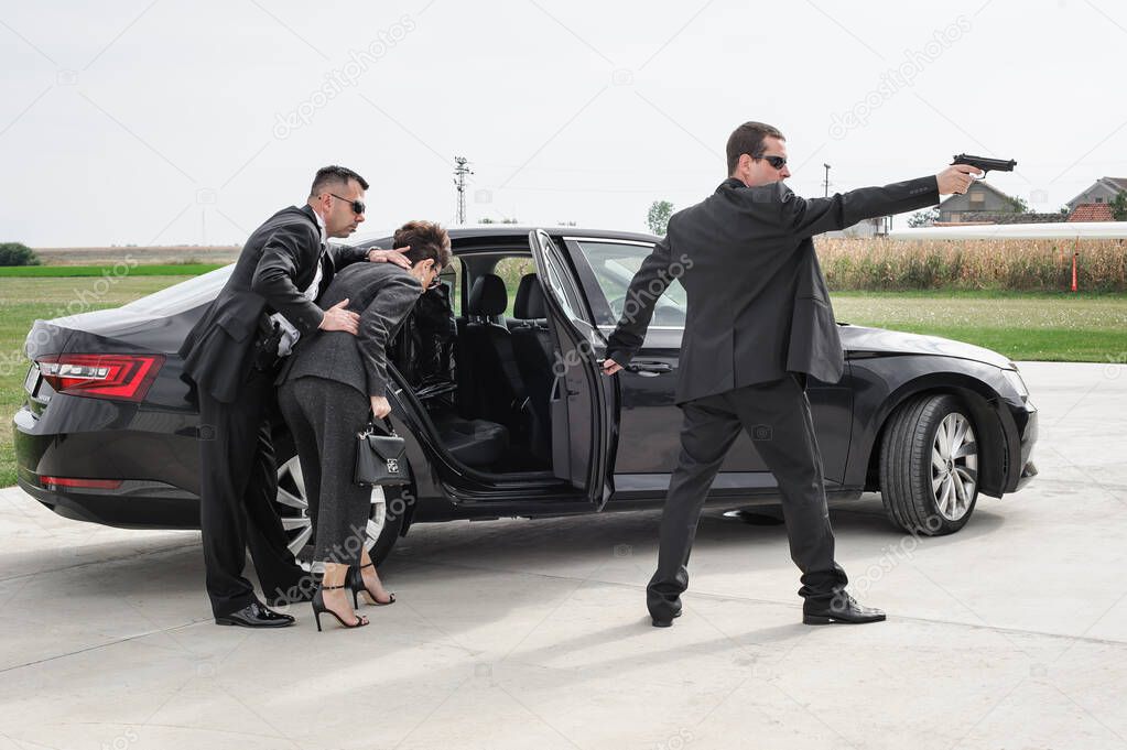 Professional armed team of female and male bodyguards protect celebrity person in car limousine. Bodyguard and VIP person security protection. Professional police agent in civilian black suit