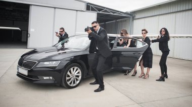 Kadın ve erkek korumalardan oluşan profesyonel silahlı bir ekip araba limuzinindeki ünlüleri koruyor. Bodyguard ve VIP kişi güvenliği. Sivil takım elbiseli profesyonel polis ajanı.