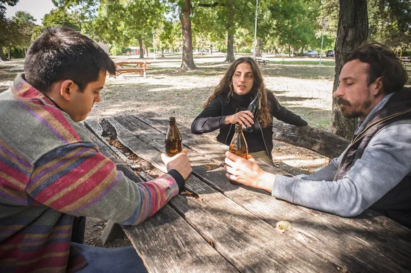 과젊은 친구들 공원의 야외에서 테이블 나무로 벤치에 병에서 맥주를 마십니다 — 스톡 사진
