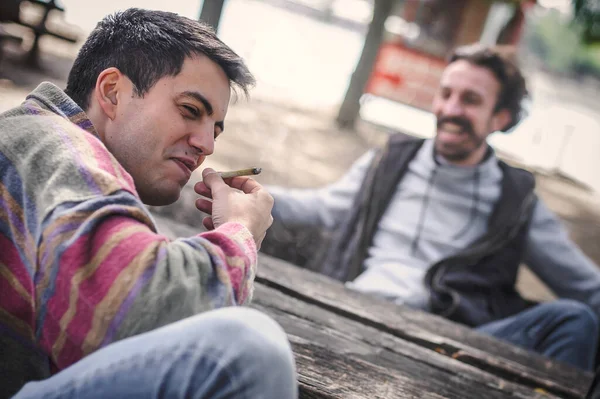 2人のリラックスした笑顔の幸せな若い友人は 屋外の公園で大麻のマリファナガンジャまたはハッシュジョイントを吸っています 二人の男が一緒にThc緑の草を吸う リアルライフシーンのコンセプト — ストック写真