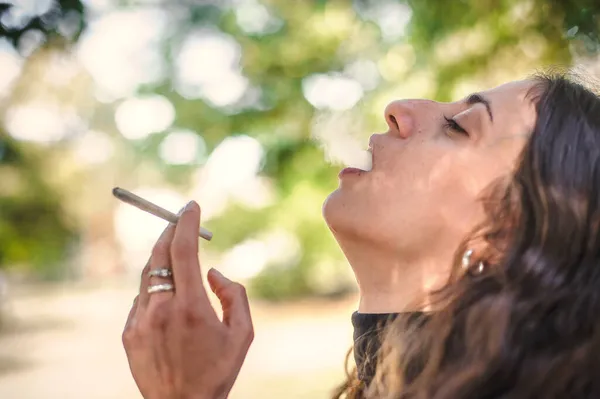 年轻女子吸食大麻大麻大麻甘贾或大麻混合香烟的特写 随便抽绿草的女青年 真实生活场景的概念 — 图库照片