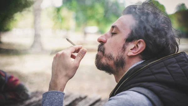 年轻男子吸食大麻大麻大麻甘贾或大麻混合香烟的特写 随随便便抽着绿草的男性 真实生活场景的概念 — 图库照片