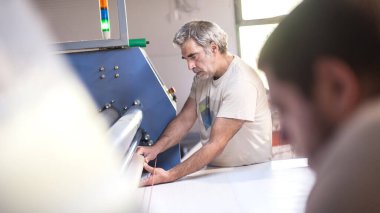 İki teknisyen işçi, dijital matbaa ofisinde büyük kaliteli endüstriyel tekstil süblimleşme Roller ısı baskı makinesi üzerinde çalışıyor.