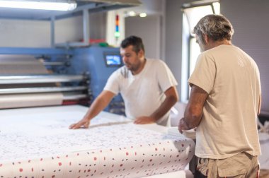 İki teknisyen işçi, dijital matbaa ofisinde büyük kaliteli endüstriyel tekstil süblimleşme Roller ısı baskı makinesi üzerinde çalışıyor.