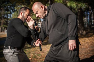 Polis eğitmeni, halka açık bir parkta polis copu kullanarak kavga, tutuklama ve tutuklama teknikleri gösteriyor. Plastik sopa, copu ya da copu.