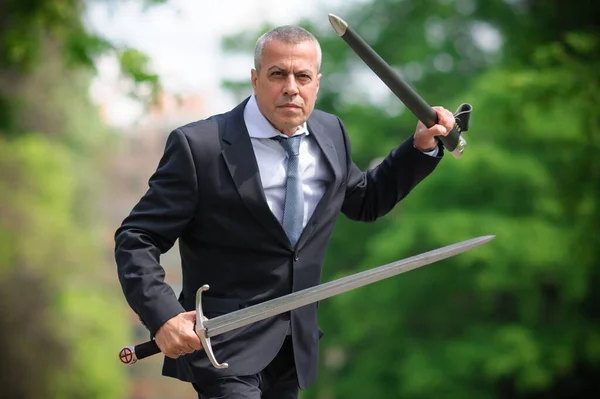 Portrait of handsome businessman model man in a modern casual suit with a large medieval sword. Modern fashion street style concept. Elegant urban warrior. Corporate and money security