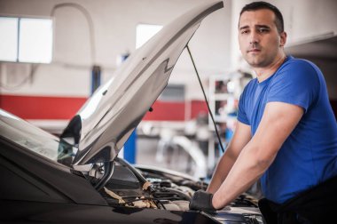 Profesyonel araba tamircisi garajda açık kapılı motoru tamir ediyor.