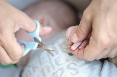 Close-up detail macro view of mom cuts the nails of a little baby with nail clippers. Hygiene and care of babies. Love and family emotion