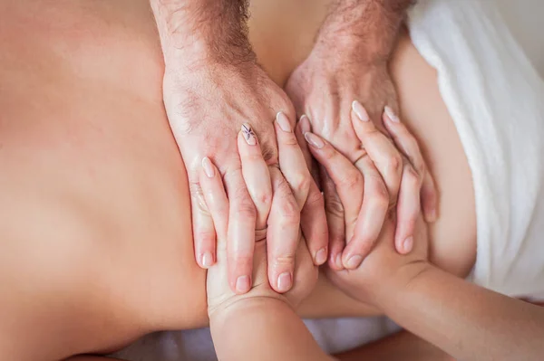 Closeup, back and hands double massage with four hands of two professional massagers for a young caucasian woman in a spa salon