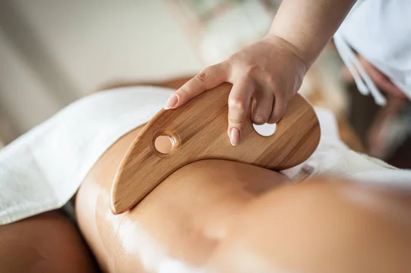 A female therapist performs maderotherapy on a woman\'s legs with a wooden massage spatula