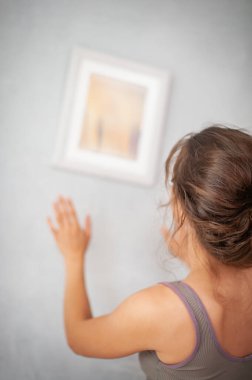 Neşeli genç bir kadın duvarda resimlerle yeni dairesini dekore ediyor.