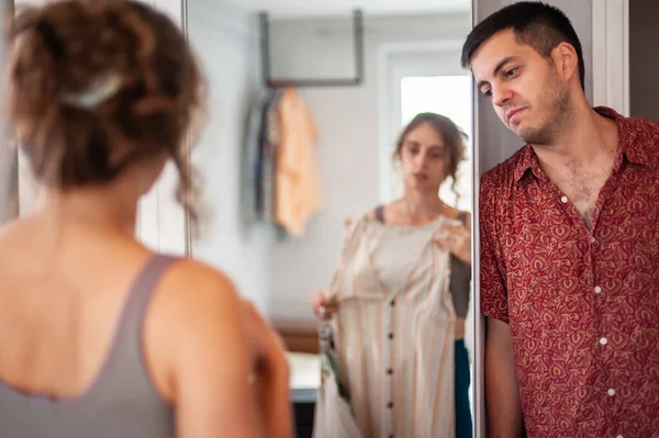 A charming young couple trying on clothes and having fun standing behind the wardrobe in the bedroom in their new apartment