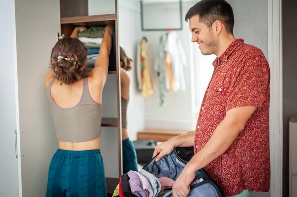 A charming young couple trying on clothes and having fun standing behind the wardrobe in the bedroom in their new apartment