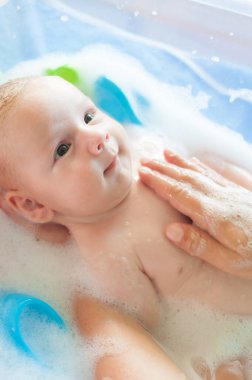 Bebek banyosu zamanı. Su ve köpüklü küvette banyo yapan anne hakkında detaylı bir görüş.
