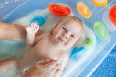 Bebek banyosu zamanı. Annesinin banyo yaparken, küvette, köpüklü ve köpüklü gülümseyen mutlu bebeğinin yakından görüntüsü.