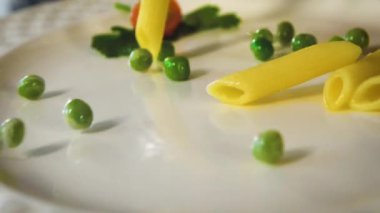 Pişmiş makarna ve sebzeler beyaz boş bir tabağa düşer..