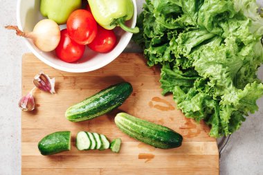 Kesme tahtasında taze sebzeler. Salata, domates, salatalık, biber, marul, soğan ve sarımsak yapmak için gerekli malzemeler..